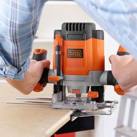 Défonceuse Black+Decker KW1200EKA en utilisation sur du bois, gros plan sur les mains manipulant l’outil.