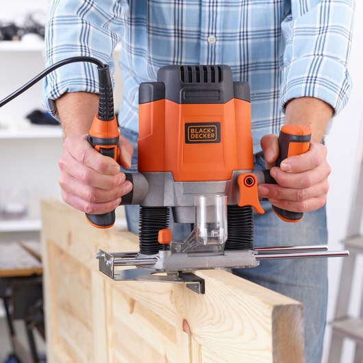 Photo de la défonceuse BLACK+DECKER KW1200EKA utilisée sur une planche, vue de face, outil orange et noir avec base transparente.