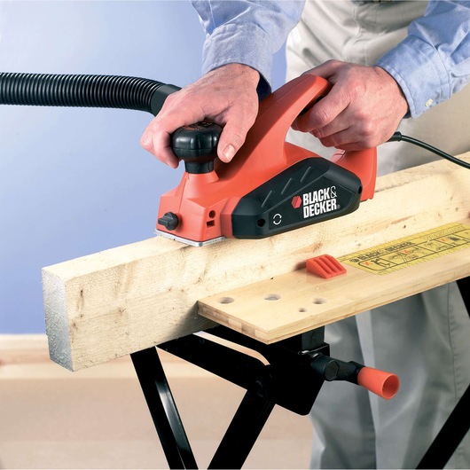 Photo de la raboteuse électrique BLACKDECKER KW712KA utilisée sur du bois, vue de côté rapprochée, outil rouge et noir.