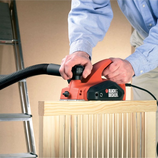 Rabot électrique BLACKDECKER KW712KA utilisé sur une surface en bois, tuyau fixé, vue rapprochée.