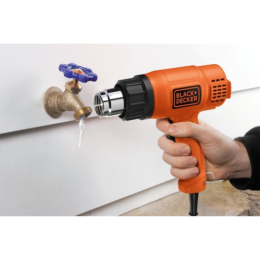 Foto van de BLACK+DECKER heteluchtpistool KX1650 die een bevroren buitenkraan ontdooit, zijaanzicht.