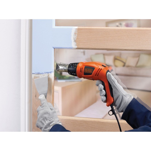 BLACKDECKER KX1693 heteluchtpistool voor het verwijderen van verf op een houten deur, close-up met handschoenen.