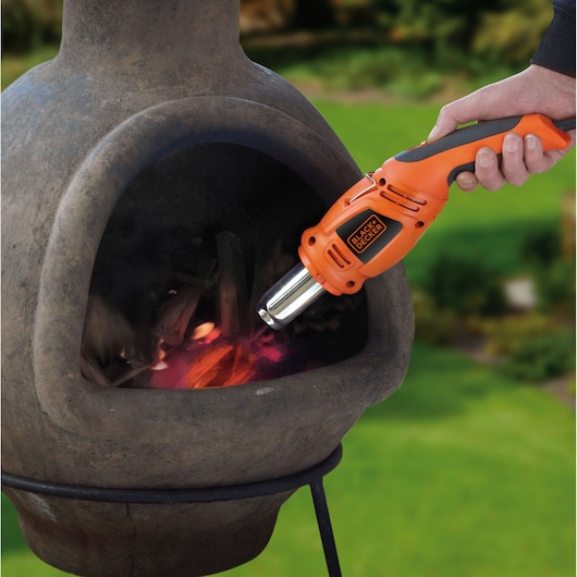 BLACKDECKER KX1693 oranje heteluchtpistool ontsteekt hout in een buitenhaard, handmatig in gebruik.