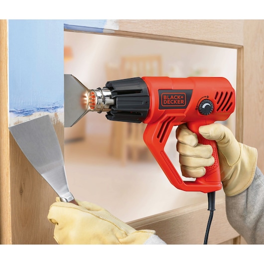 BLACKDECKER KX2001K heteluchtpistool wordt gebruikt voor verfverwijdering, close-up van gereedschap en handschoenen.