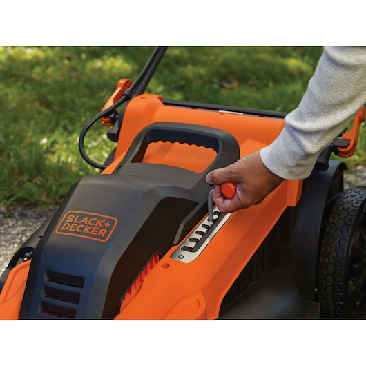 Foto van BLACK+DECKER LM2000 grasmaaier met hendel voor hoogteverstelling in gebruik, oranje en zwarte behuizing.