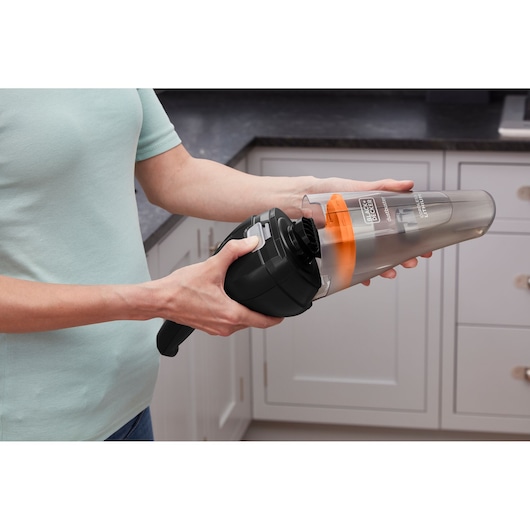 Persoon leegt BLACKDECKER handstofzuiger NVC115BJL met doorzichtige stofcontainer in een keuken.