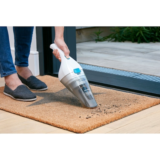 Aspirateur à main BLACKDECKER NVC115JL utilisé pour nettoyer la saleté sur un paillasson à l'intérieur.