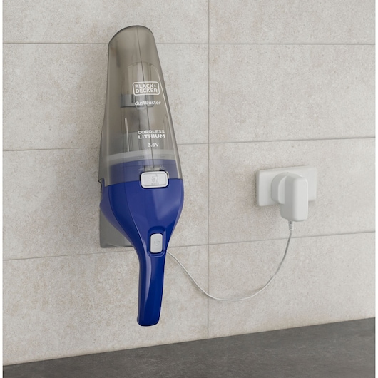 BLACK+DECKER NVC115WA handstofzuiger met blauwe handgreep, aan de muur bevestigd en opladend via witte stekker.