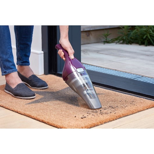BLACK+DECKER NVC115W handstofzuiger, paars en grijs, gebruikt om vuil op een deurmat te reinigen.