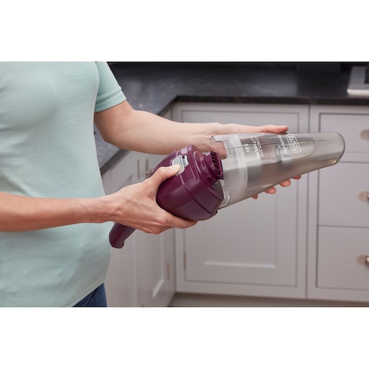 Paarse BLACKDECKER NVC115W handstofzuiger vastgehouden door een persoon in een keuken, stofreservoir wordt verwijderd.