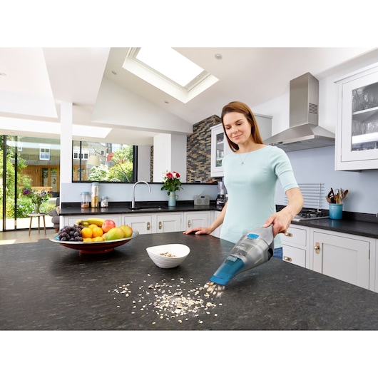 BLACK+DECKER NVC215WA handstofzuiger zuigt havermout op aanrecht bij fruitschaal en ontbijtkom.
