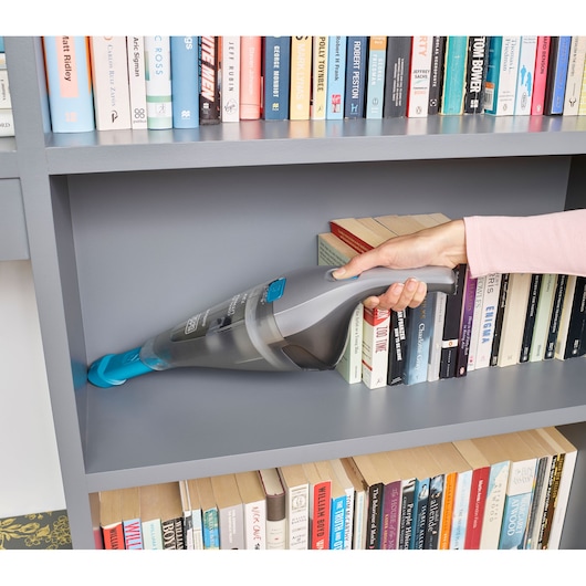 BLACK+DECKER NVC215WA handstofzuiger met blauwe mondstuk reinigt grijze boekenkast, boeken op de achtergrond.