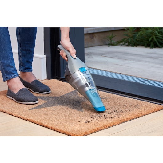 BLACKDECKER NVC215WA handstofzuiger reinigt vuil van een deurmat binnen.