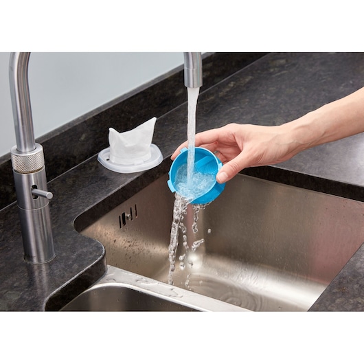 BLACKDECKER NVC215WA blauwe stofzuigerfilter wordt afgespoeld onder stromend water in een keukenspoelbak, zijaanzicht.