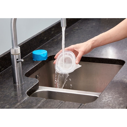 Foto van het schoonmaken van de BLACKDECKER NVC215WA stofzuigerfilter onder stromend water in de gootsteen.