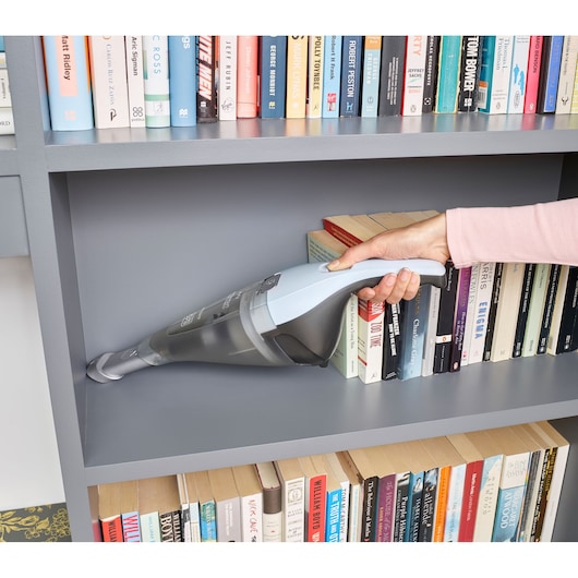 BLACKDECKER NVC215W handstofzuiger reinigt een grijze boekenplank naast boeken, close-up zijaanzicht.