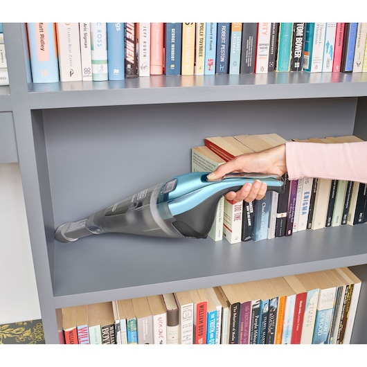 Foto van BLACKDECKER NVC220WBC handstofzuiger reinigt grijze boekenkast bij boeken.