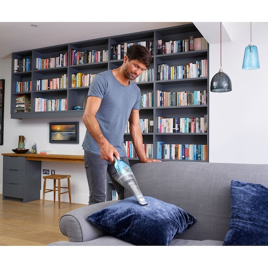 BLACKDECKER NVC220WBC handstofzuiger gebruikt op grijze bank met blauw kussen in moderne woonkamer