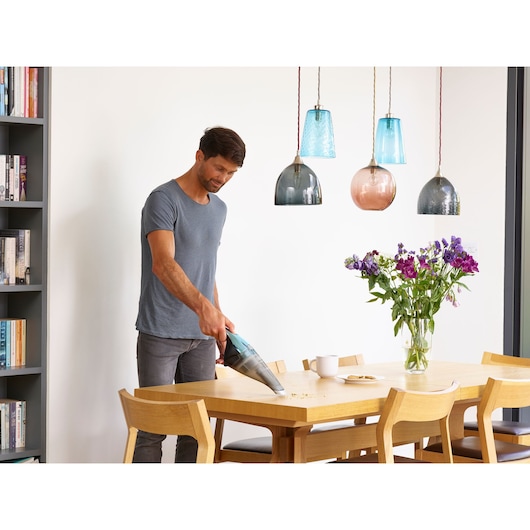 BLACK+DECKER NVC220WBC handstofzuiger verwijdert kruimels van eettafel in moderne keuken.