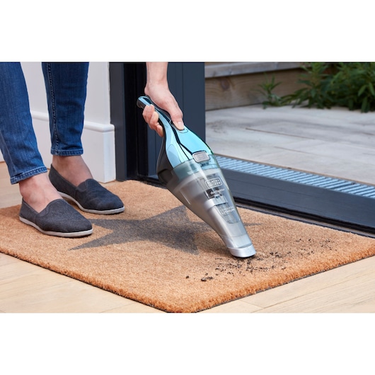 BLACKDECKER NVC220WBC handstofzuiger reinigt vuil op een deurmat bij een deuropening.
