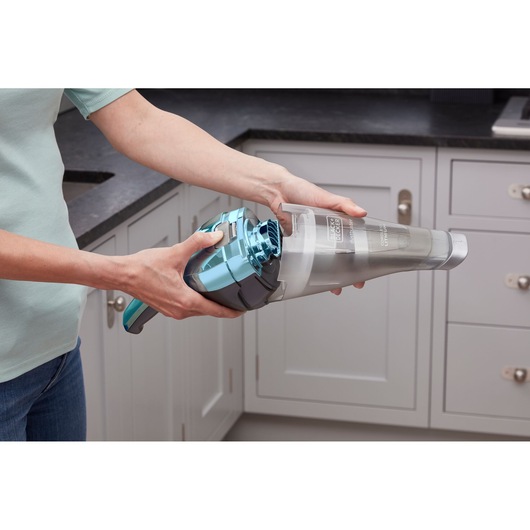 Persoon gebruikt BLACKDECKER NVC220WBC handstofzuiger in een keuken.