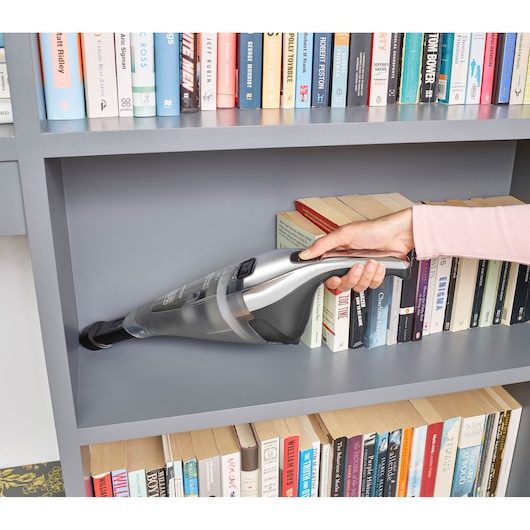 BLACKDECKER NVC220WC handstofzuiger reinigt boekenplank, zilver en zwart, zijaanzicht.
