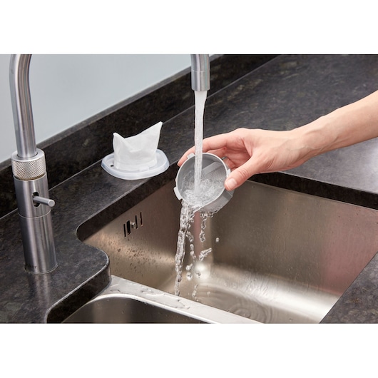 Foto van BLACKDECKER NVC220WC stofzuigerfilter die onder stromend water in een keukenspoelbak wordt schoongemaakt.