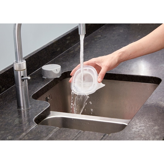 Foto van BLACKDECKER NVC220WC stofzuigerfilter die wordt afgespoeld met water in een keukengootsteen.