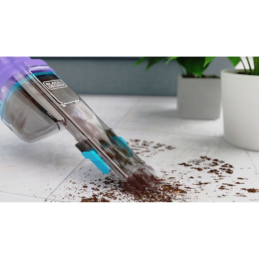 BLACK+DECKER NVD220BP handstofzuiger zuigt vuil op van witte vloer, met planten in pot op de achtergrond.