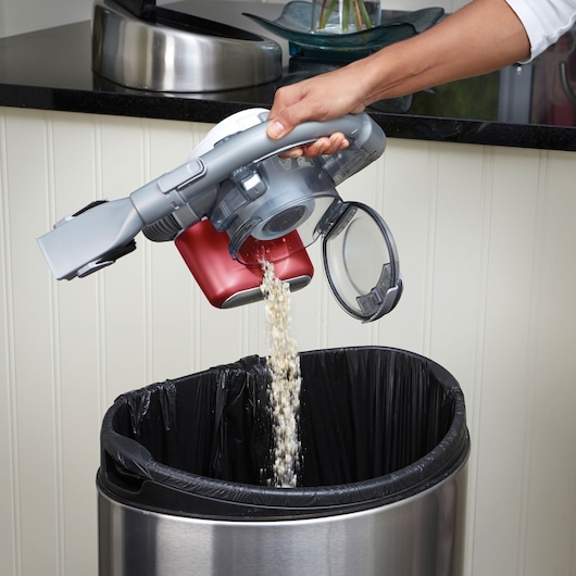 Aspirateur à main BLACKDECKER PD1020L vidé dans une poubelle, bac à poussière ouvert et corps rouge visible.