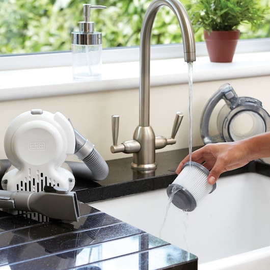 Filtre d’aspirateur à main BLACKDECKER PD1020L rincé sous le robinet, pièces d’aspirateur sur le comptoir.