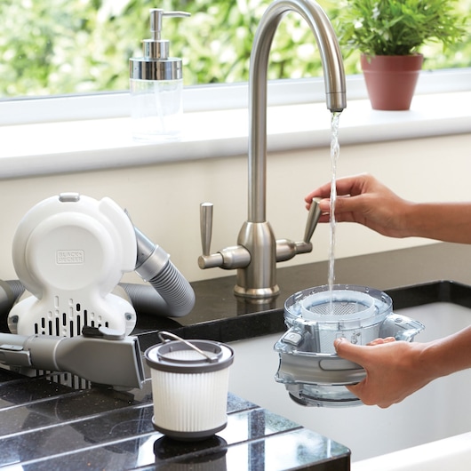 Photo du filtre et du réservoir de l’aspirateur à main BLACKDECKER PD1020L nettoyés sous un robinet, pièces sur comptoir noir.