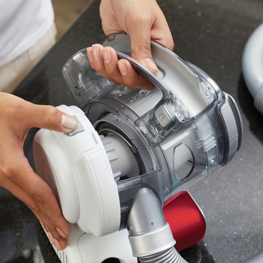 Photo en gros plan de l'aspirateur à main BLACKDECKER PD1020L avec une personne ouvrant le bac à poussière.