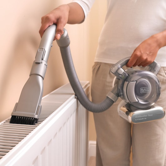 Aspirateur à main BLACKDECKER PD1820L nettoyant un radiateur avec flexible et brosse.