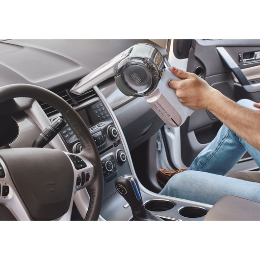 Photo de l’aspirateur à main BLACK+DECKER PV1820LRGP utilisé pour nettoyer la grille de ventilation du tableau de bord d’une voiture.