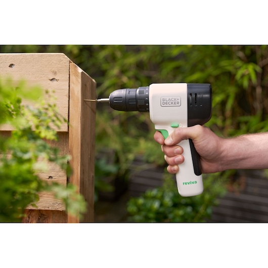 Perceuse sans fil BLACK+DECKER REVDD12C vissant une vis dans une planche en bois en extérieur.