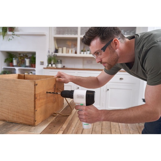 Perceuse sans fil BLACKDECKER REVDD12C utilisée sur une boîte en bois dans une cuisine.