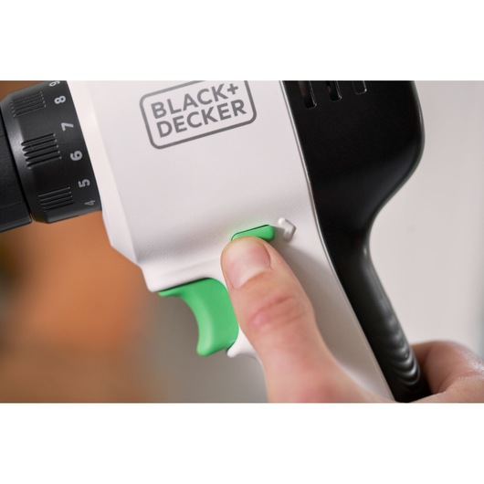 Photo en gros plan de la poignée de la perceuse BLACK+DECKER REVDD12C avec une main appuyant sur l’interrupteur vert.