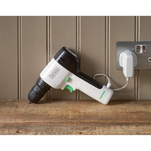 Photo de la perceuse sans fil BLACK+DECKER REVDD12C noir et blanc, en charge sur une surface en bois près d'une prise murale.
