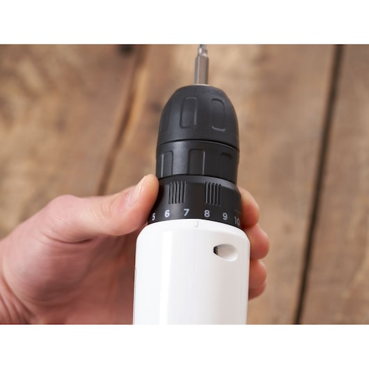 Photo rapprochée de la perceuse sans fil BLACKDECKER REVDD12C, main réglant le couple, fond en bois.