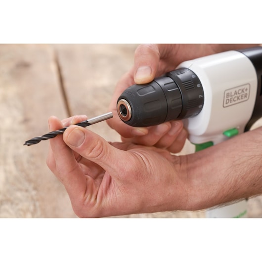 Mains insérant un foret dans la perceuse sans fil BLACK+DECKER REVDD12C, vue rapprochée sur surface en bois.