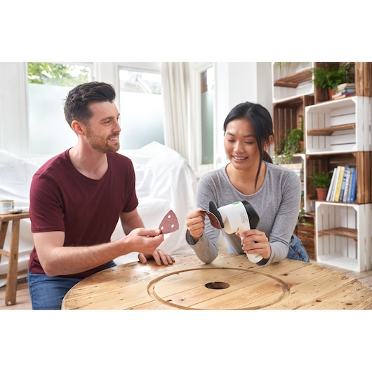 Photo de la ponceuse BLACKDECKER REVDS12C tenue par une personne, avec feuille abrasive, déco intérieure.
