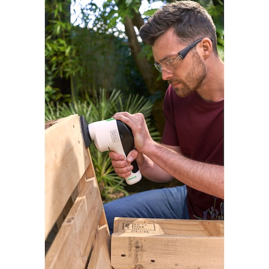 Ponceuse BLACK+DECKER REVDS12C utilisée sur une palette en bois à l'extérieur.
