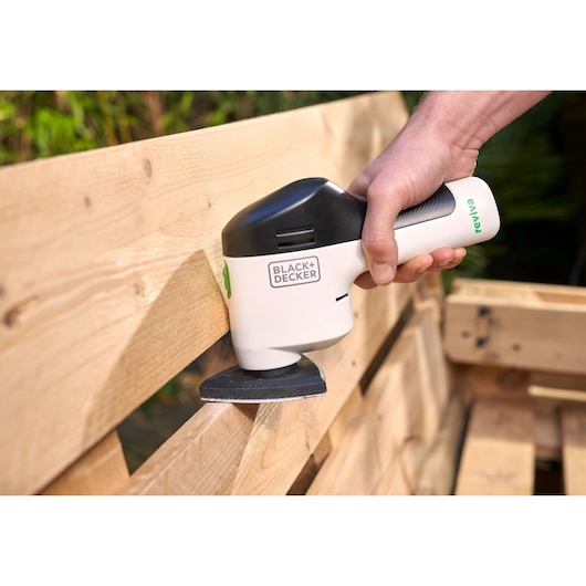 Photo de la ponceuse portative BLACK+DECKER REVDS12C utilisée sur une palette en bois.