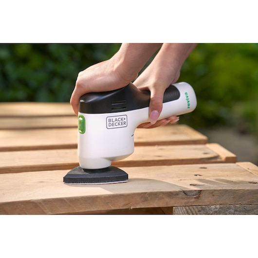 Ponceuse de détail sans fil BLACK+DECKER REVDS12C utilisée sur du bois, tenue à la main, en extérieur.