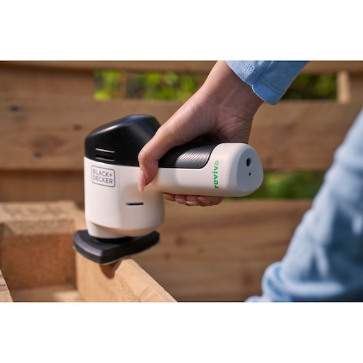 Ponceuse de détail sans fil BLACK+DECKER REVDS12C utilisée sur un coin en bois, noire et blanche, tenue à la main.