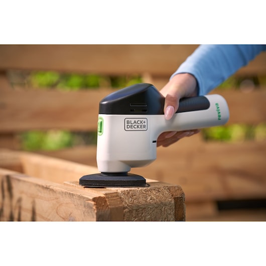 BLACK+DECKER REVDS12C ponceuse portative utilisée sur du bois à l'extérieur, tenue en main.