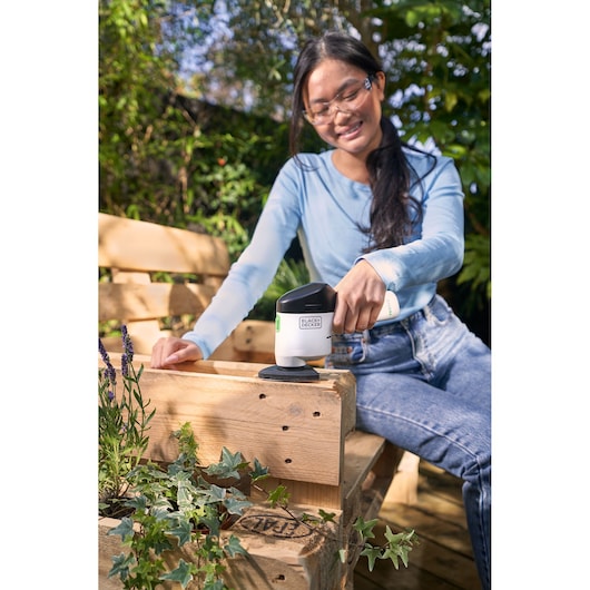 BLACK+DECKER REVDS12C ponceuse sans fil utilisée à l’extérieur sur un banc en bois.