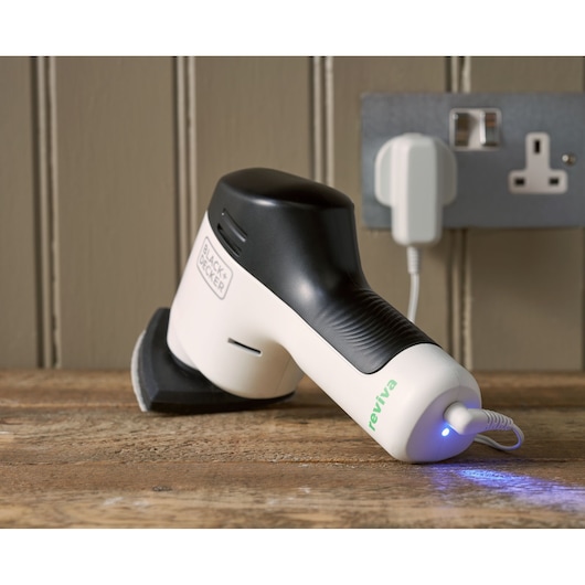 BLACK+DECKER REVDS12C ponceuse à main sur surface en bois, design blanc et noir, en charge avec voyant bleu.