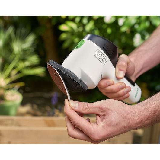 Photo de ponceuse de précision BLACK+DECKER REVDS12C tenue à la main, papier abrasif fixé sur le plateau.